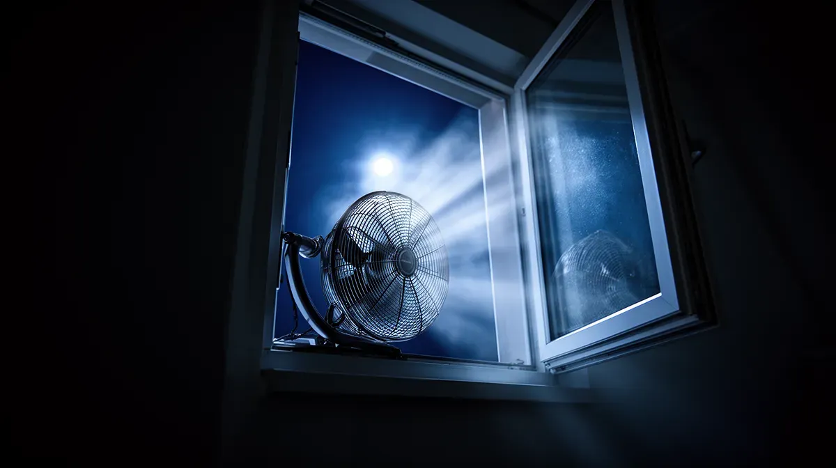 Ventilateur placé devant une fenêtre ouverte la nuit pour expulser l'air chaud et créer un courant d'air frais.